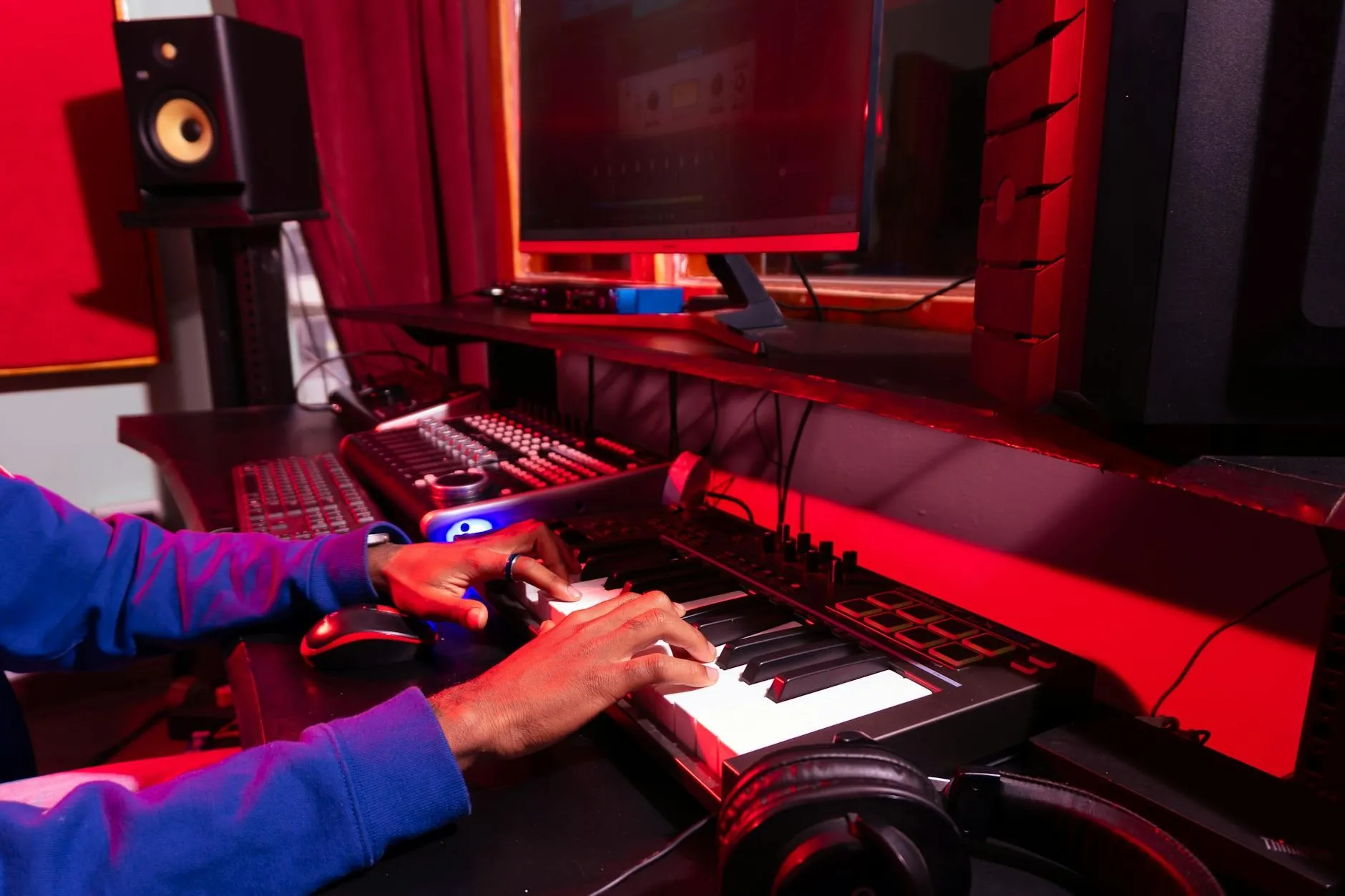 Person spielt ein MIDI-Keyboard in einem Studio mit Kopfhörern und Studiomonitor